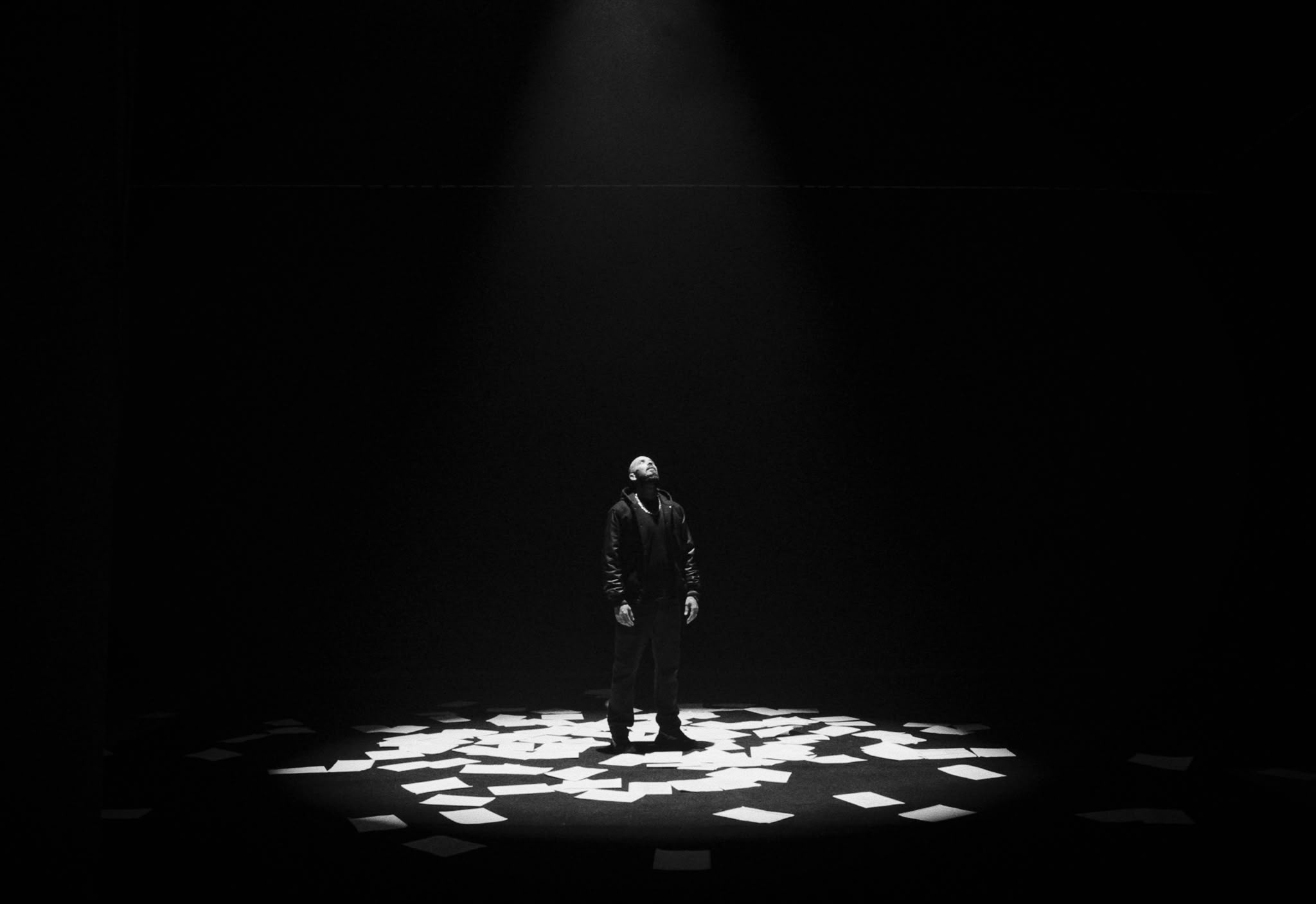 Figure seule sous un projecteur, feuilles blanches au sol.